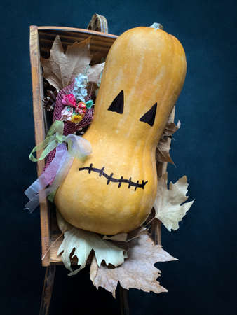Halloween pumpkin with a bouquet lying in a wooden cart over autumn leaves on a dark backgroundの写真素材