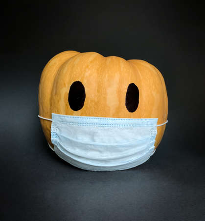 Halloween 2020 pandemic protective face mask on orange pumpkin over dark gray backgroundの写真素材