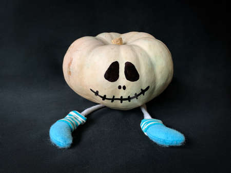 Cute Halloween white pumpkin with painted  jack o lantern face and legs with socks on black backgroundの写真素材
