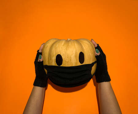 Halloween pumpkin covered with face mask against coronavirus or covid-19 holded by handsの写真素材