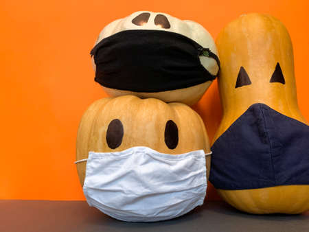 Close Up view of Halloween pumpkins with a protective masks due to Coronavirus on a orange backgroundの写真素材