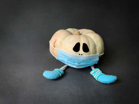 Coronavirus Halloween cute pumpkin with a legs wearing socks and medical mask sitting on dark backgroundの写真素材