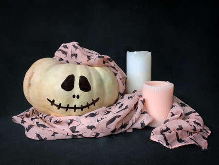 Cute white Halloween pumpkin with a pink scarf over it next to white and pink candles on black backgroundの写真素材
