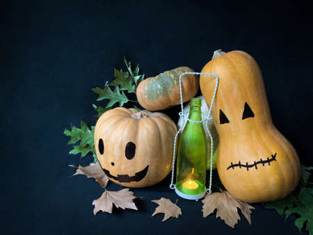 Still life Halloween pumpkins with a glowing candle in a bottle and autumn leaves on dark backgroundの写真素材