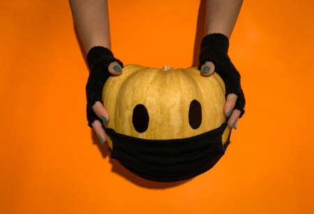 Hands with fingerless gloves holding Halloween pumpkin wearing a face mask as protection against coronavirus or covid-19の写真素材