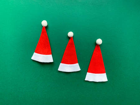 Three Christmas hats composition on green background. Top view with copy space.