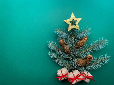 Abstract Christmas tree made of spruce branch with pine cones and golden star on top. Flat lay green...