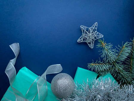 Christmas gifts with silver ribbon, silver ball, star, garland decorations and green branch on blue background. Flat lay Christmas, Holiday frame, banner, card with copy space.の写真素材