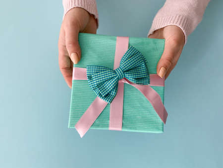 Female hands holding beautiful turquoise present with soft silk pink ribbon over light blue background.の写真素材