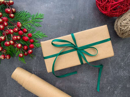 Festive elegant gift box decorated with green ribbon, fir tree and red berries branches on wooden background with balls and craft paper.の写真素材