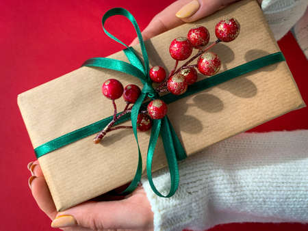 Brown craft paper present with green ribbon and branch of berries in hands. Present making for give in holidays or special day.の写真素材