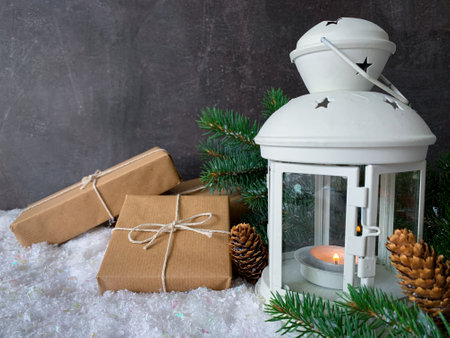 Brown paper christmas gift box with pine branches and white lantern on snow over dark texture surface background.の写真素材