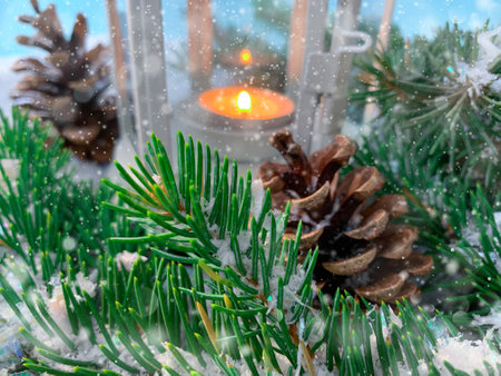 Pine tree branches with cones on a snowy background with candle lamp in distance. Blurred background magic of the holiday.の写真素材