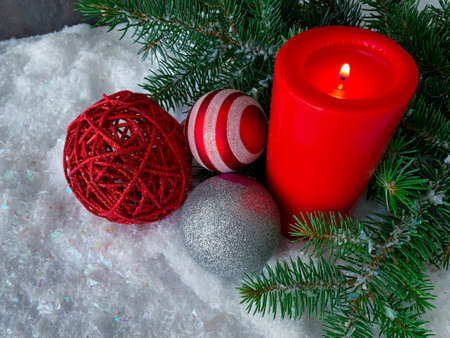 High angle view of burning red candle, Christmas baubles with fir tree on snowy background.の写真素材