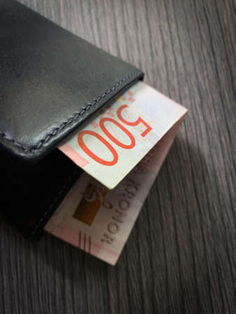 500 Swedish krona bill in black leather wallet. Close up photo of wallet with money isolated on dark...