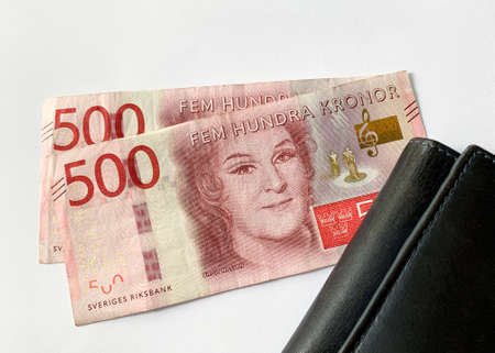 Close up view of two Swedish money banknotes next to a black leather wallet isolated on white background.の写真素材
