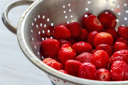 Fresh strawberries in stainless steel colander white wooden background