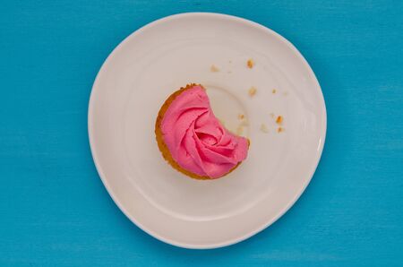 Pink bitten cupcake on a plate isolated on blue background. Delicious cakeの写真素材