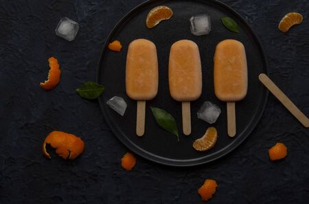Homemade orange ice pop with ice and citrus fruits on blackの写真素材