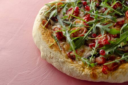 Vegan pizza with fresh garnet and arugula leaves on colored