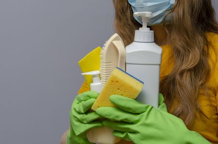 woman with a medical face mask and latex gloves holding cleaning supplies. Corona virus pandemic.の写真素材