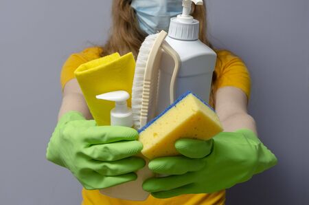 woman with a medical face mask and latex gloves holding cleaning supplies. Corona virus pandemic.の写真素材