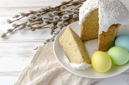 Kulich Easter cake with colored eggs with white glaze on white wooden background