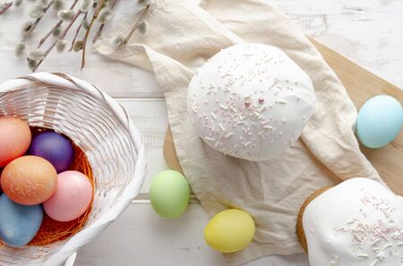 Kulich Easter cake with colored eggs with white glaze on white wooden background