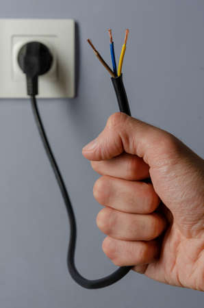 Unplug or plugged in concept, a hand holds an electrical cable plugged into an outletの写真素材