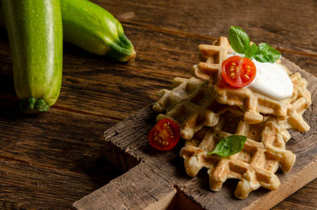 vegetarian zucchini waffles with herbs on a plate with fresh tomatoes, basil and sour cream on a wooden background.の写真素材