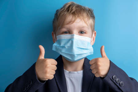 Portrait of school boy with face mask and school uniform. Blue backgroundの写真素材