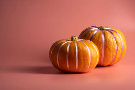 Pumpkins on pastel pink background with pastel ribbon. Autumn, fall, halloween concept.の写真素材