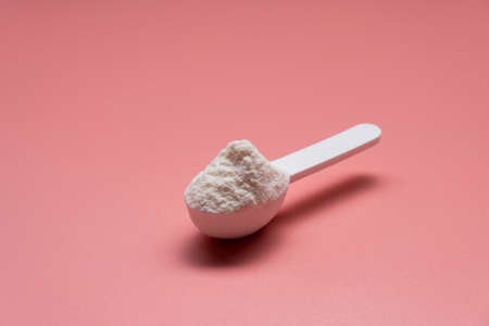 White collagen powder on a plastic measure spoon on a pink background.の写真素材