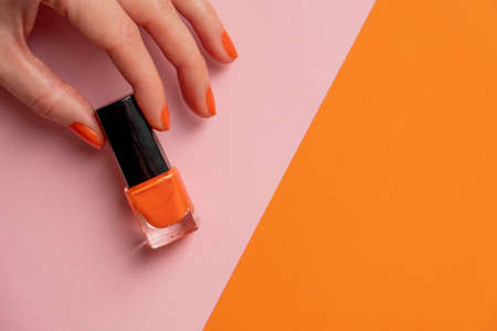 Woman hand hold orange lacquer on orange pink background. Female hand with orange nail.の写真素材