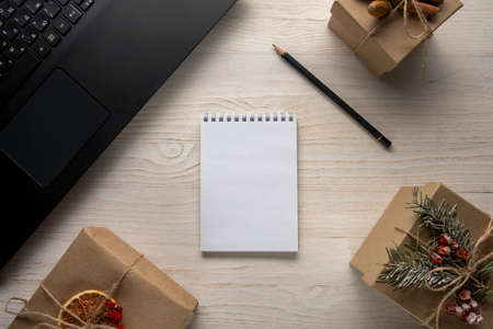 Wish or shopping list concept. White paper notepad on wooden background with gift and fir tree