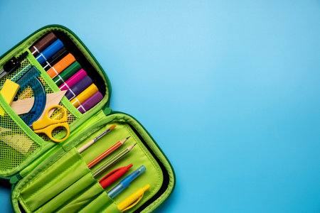 Green school pencil case. Colored different school supplies in case on blue background. Back to school concept. Flat lay, top view, copy spaceの写真素材