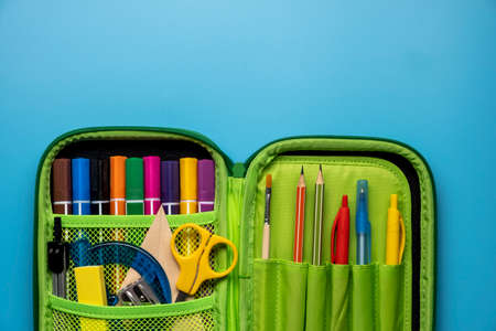 Green school pencil case. Colored different school supplies in case on blue background. Back to school concept. Flat lay, top view, copy spaceの写真素材