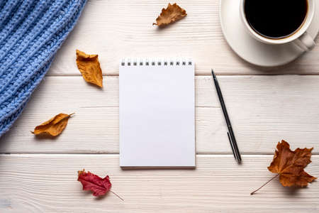 Cup of coffee, plaid, notepad, autumn leaves on white wooden background.