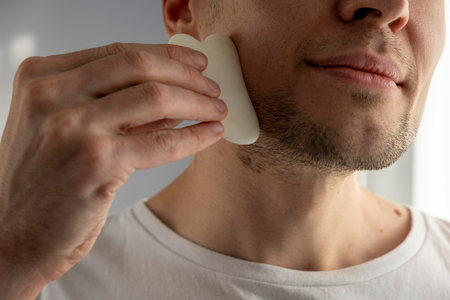 Bearded man is using jade face stone at home for beauty facial massage therapy.の写真素材