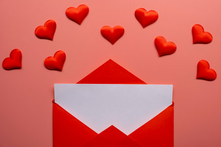 Red paper envelope with blank white note mockup inside and Valentines hearts on pink background.