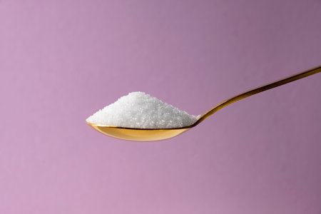 Erythritol in a golden spoon on a lilac background. Diet, healthy food concept.の写真素材