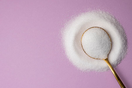 Erythritol in a golden spoon on a lilac background. Diet, healthy food concept.の写真素材