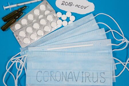 Medicines against Coronavirus model. Different pills, syringes, text CORONAVIRUS. 2019 nCoV coronavirus on blue background.の写真素材