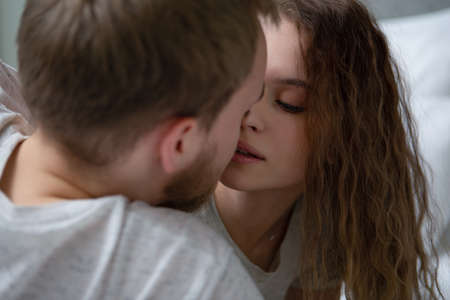 Beautiful young couple gently kissing lying in bed. Loving each other man and womanの写真素材
