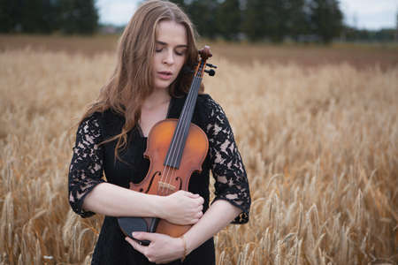 a sad young woman violinist with downcast eyes gently presses her violin to herの写真素材