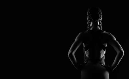 A brutal athletic woman with pumped-up muscles stands with her hands on her hips. Black and white photo