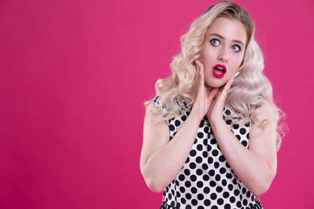Portrait of a beautiful surprised woman. A charming girl with perfect makeup is excited and opened her mouth in surprise. Shot in the head. Emotions. Isolated on a pink backgroundの写真素材