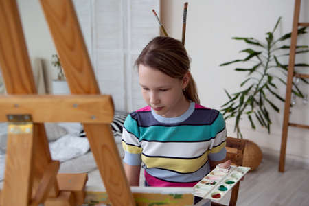 a charming girl artist enthusiastically paints a picture sitting at an easelの写真素材