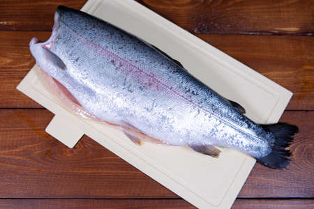 A headless peeled trout lies on a chopping Board against a dark wooden background
