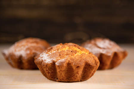 Freshly baked delicious cupcakes in powdered sugar on a wooden table. Freshly made cake